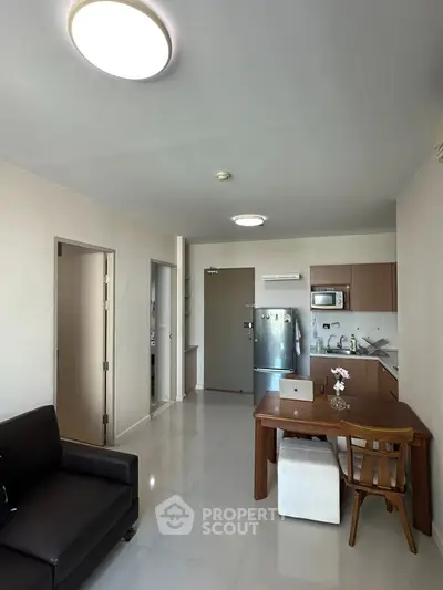 Modern open-plan living room with kitchen, featuring sleek furniture and stainless steel appliances.