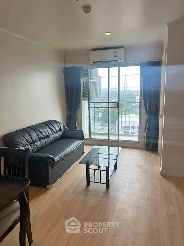 Bright living room with modern sofa and glass coffee table, featuring a large window with city view.