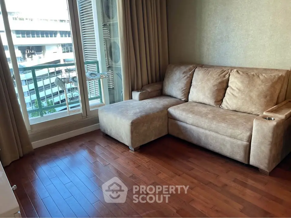 Cozy living room with plush sofa and wooden flooring, featuring a view of the cityscape through large windows.