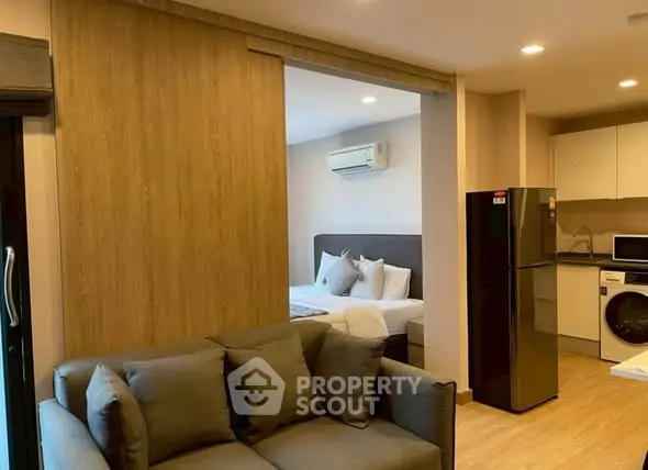 Modern apartment interior with cozy living room and open kitchen layout, featuring a washing machine and fridge.