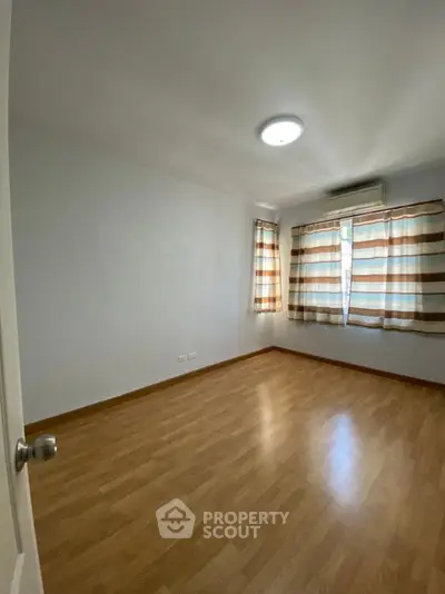 Spacious empty bedroom with wooden flooring and striped curtains, ready for personalization.