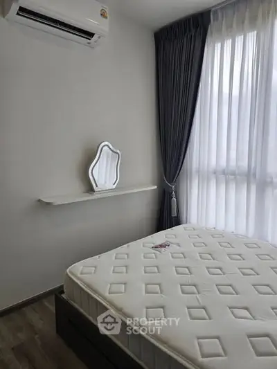 Modern bedroom with air conditioning and natural light, featuring a stylish mirror and elegant curtains.