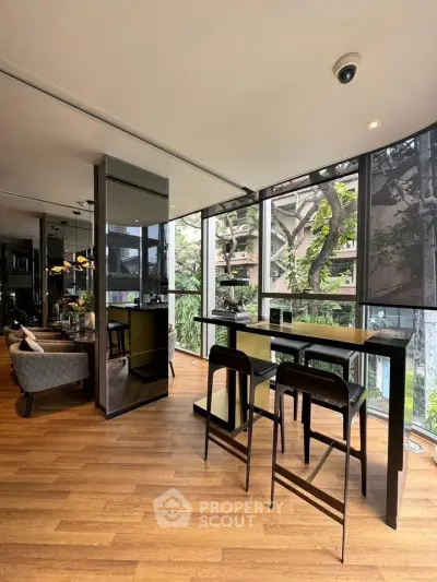 Modern living room with floor-to-ceiling windows and stylish furniture, offering a lush green view.