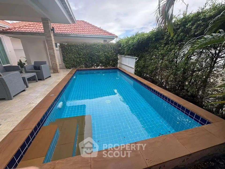 Charming private pool with lush greenery and cozy patio seating in a serene residential setting.