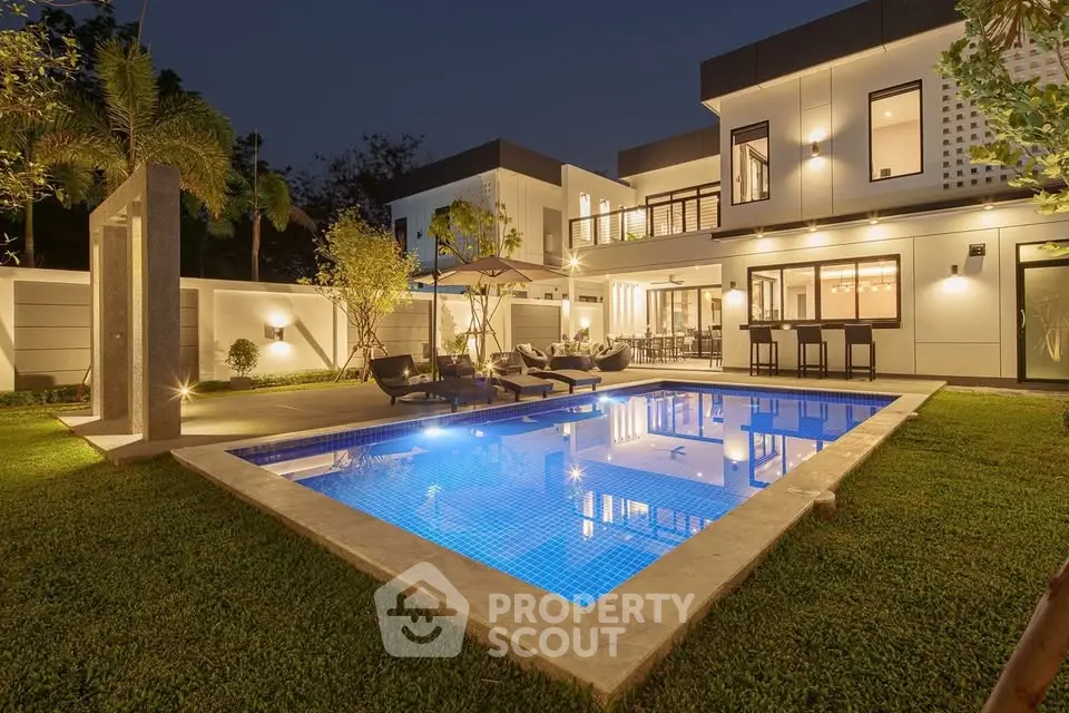 Luxurious modern home with illuminated pool and stylish outdoor seating area at dusk.