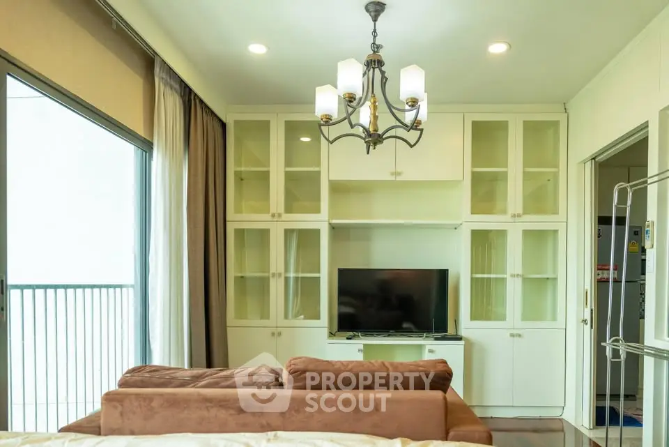 Spacious living room with elegant chandelier and built-in TV cabinet, featuring a cozy brown sofa and large sliding glass doors.