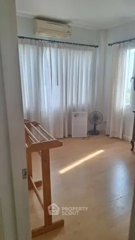 Bright room with wooden floors, air conditioning, and large windows with curtains.