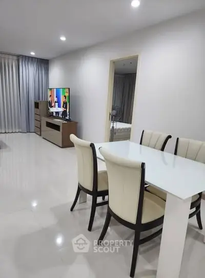 Modern living room with sleek dining area and TV, featuring elegant furniture and bright lighting.