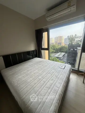 Cozy bedroom with large window offering city view and air conditioning unit.