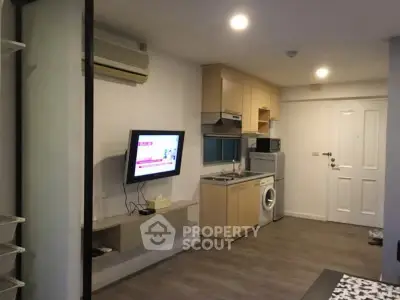 Modern apartment interior with compact kitchen and living area, featuring a washing machine and wall-mounted TV.