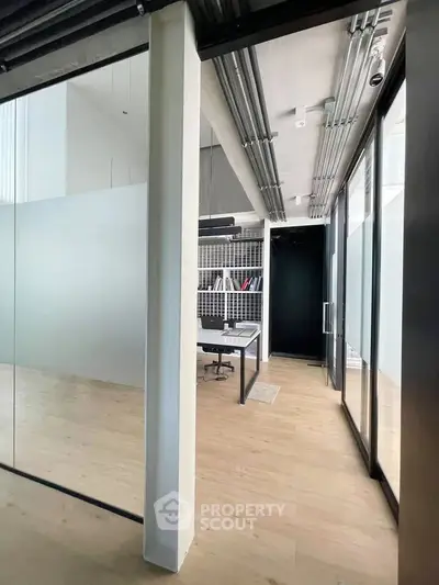 Modern office space with glass walls and sleek design, featuring a minimalist desk and shelving.