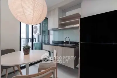 Modern kitchen with sleek design and dining area, featuring black fridge and stylish lighting.
