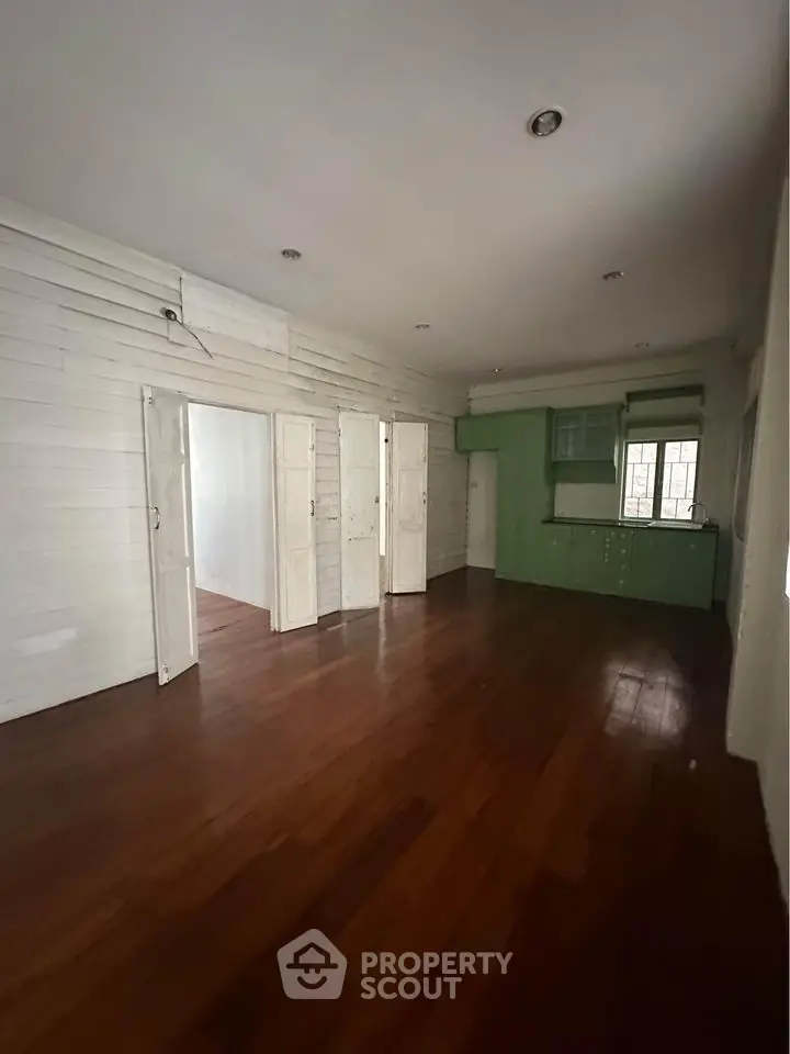 Spacious open-plan living area with wooden flooring and green kitchen cabinets.