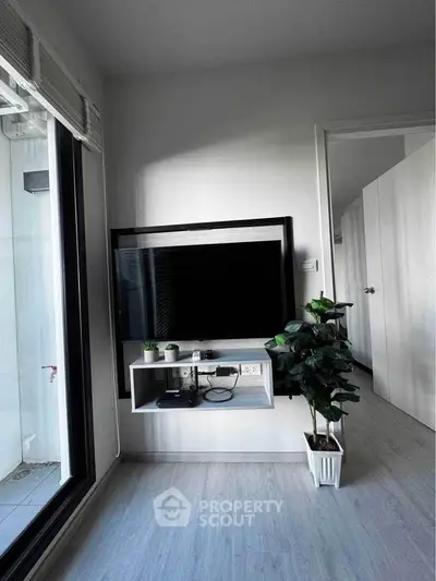Modern living room with sleek TV setup and potted plant, featuring minimalist decor and natural light.