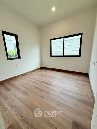 Spacious empty room with wooden flooring and large windows, perfect for customization.