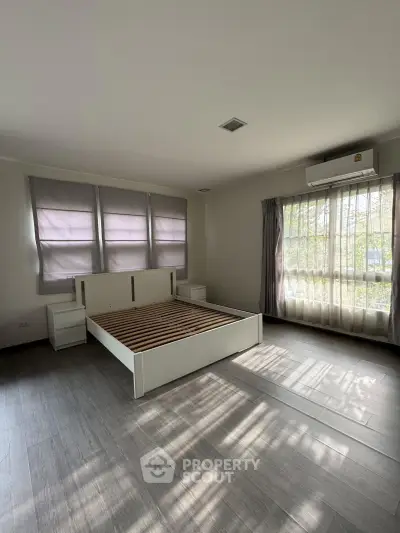 Spacious bedroom with large windows and natural light, featuring a modern bed frame and elegant flooring.