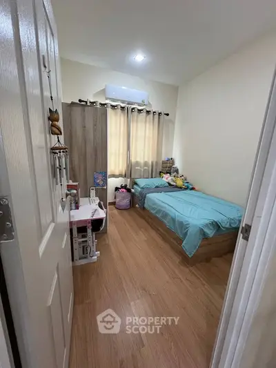 Cozy bedroom with wooden flooring and natural light, perfect for relaxation and comfort.