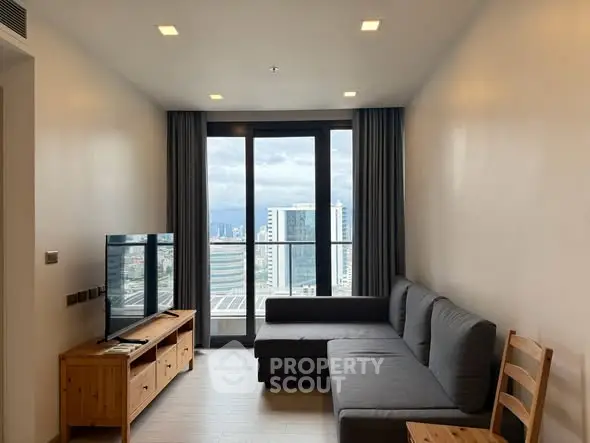 Modern living room with large windows and city view, featuring a stylish gray sofa and wooden furniture.