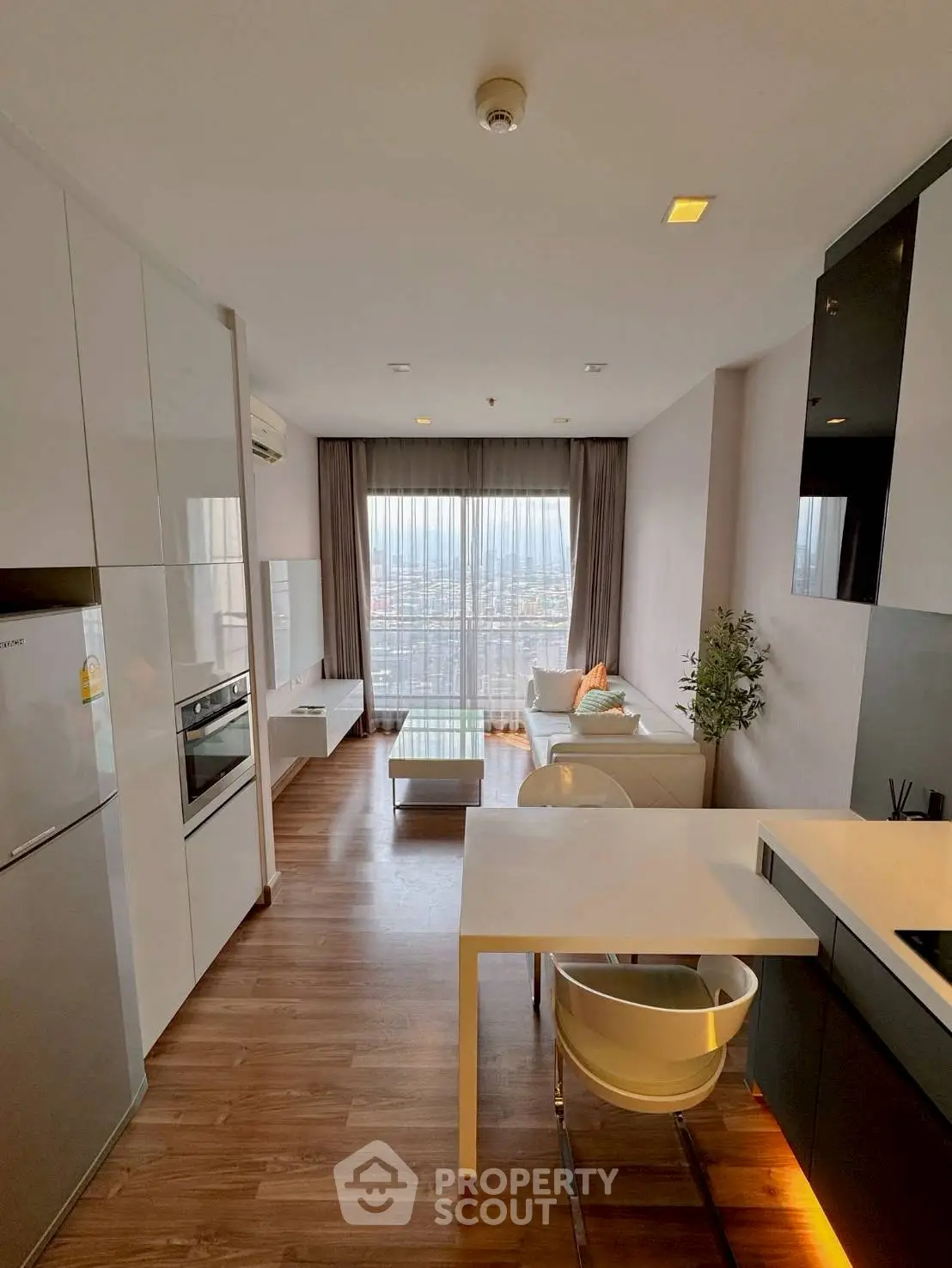 Modern open-layout living room with kitchen, featuring sleek furniture and large windows with city view.