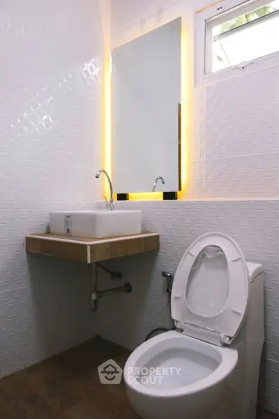 Modern bathroom with sleek sink and toilet, featuring stylish wall tiles and ambient lighting.