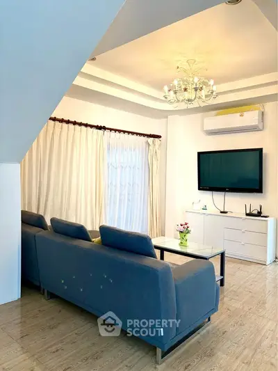 Elegant living room with modern decor, featuring a cozy sofa, flat-screen TV, and stylish chandelier.