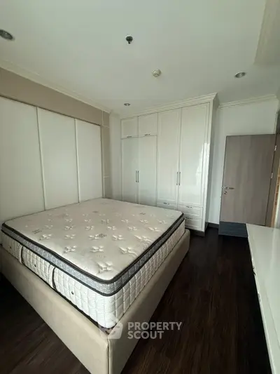 Spacious bedroom with elegant hardwood flooring and built-in wardrobe, featuring a comfortable mattress.