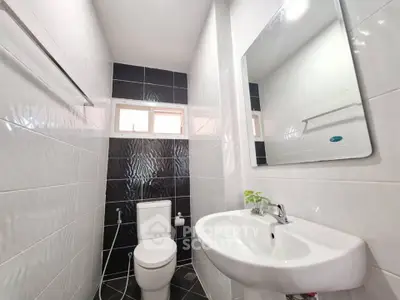 Modern bathroom with sleek black and white tiles, featuring a compact design and a large mirror.