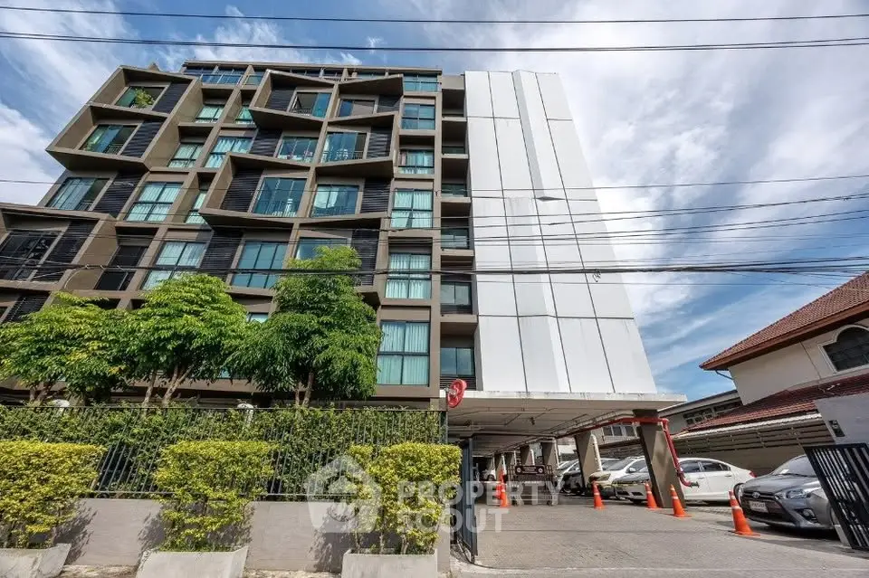 Modern apartment building with spacious parking area and lush greenery, ideal for urban living.