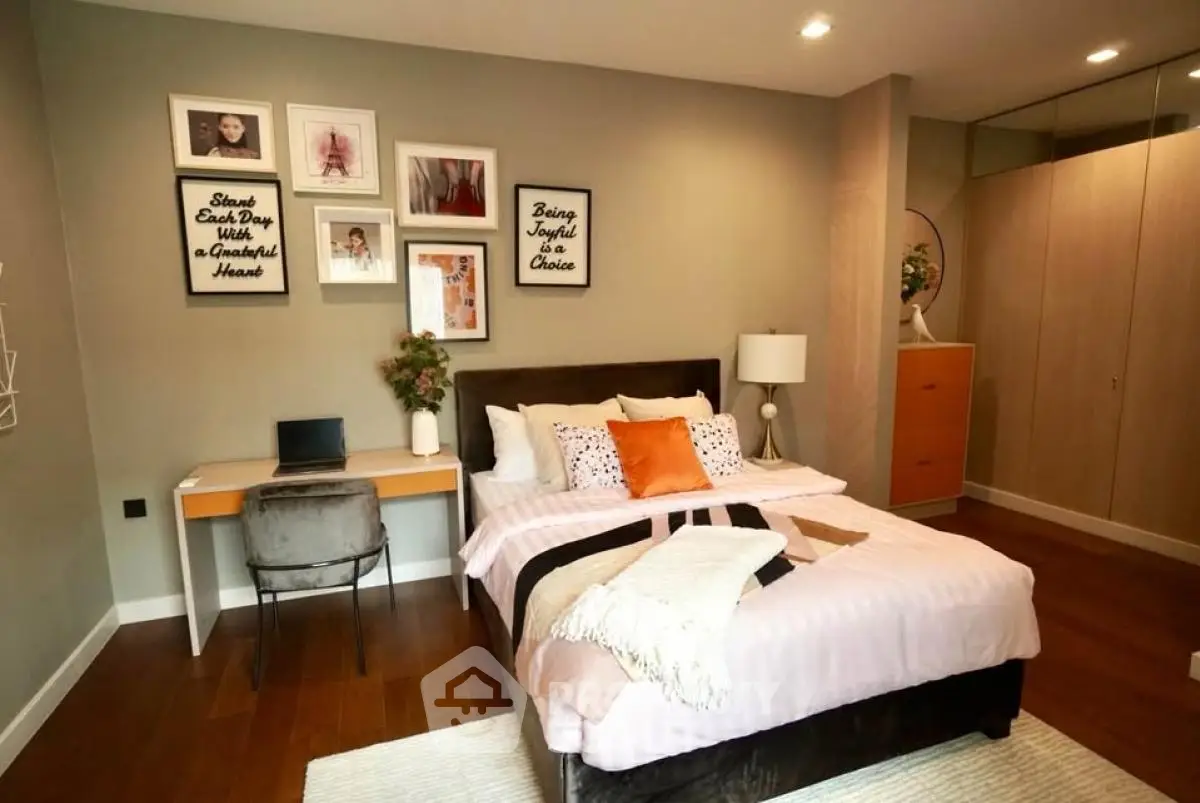 Cozy bedroom with stylish decor and workspace, featuring wooden flooring and modern furniture.