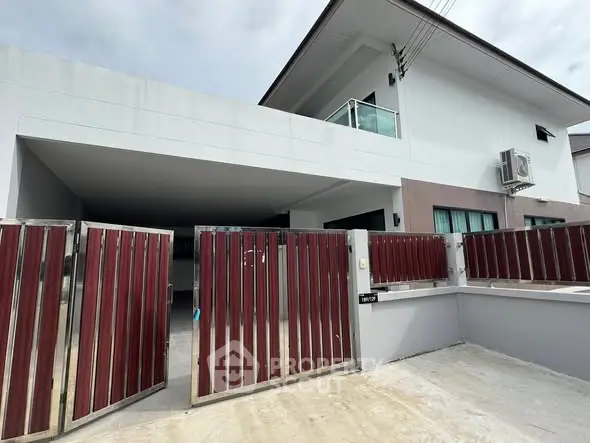Modern two-story house with gated entrance and balcony in a suburban setting.