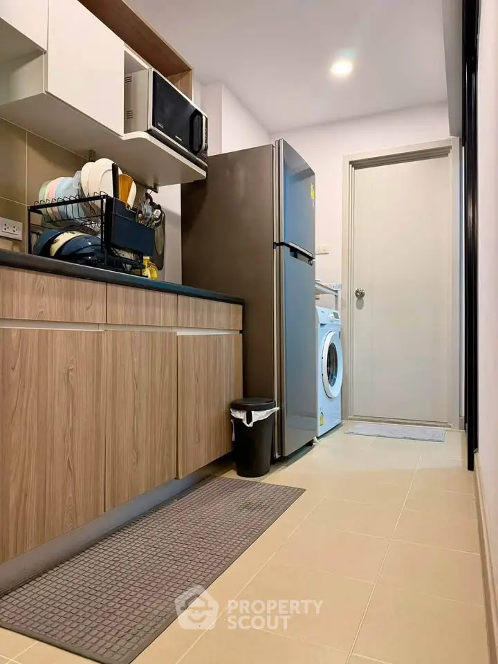 Modern kitchen with wooden cabinets, stainless steel fridge, and washing machine in a cozy apartment.