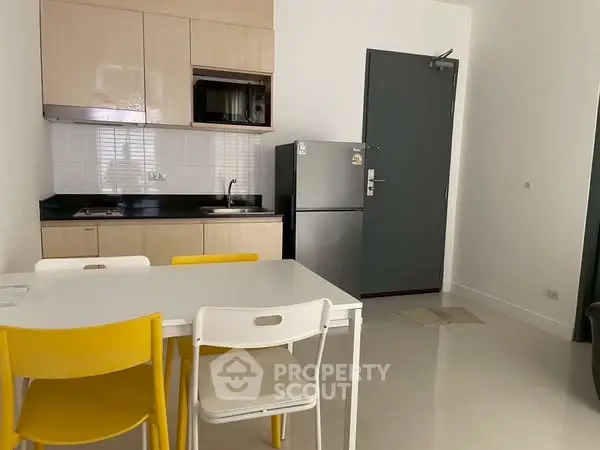 Modern compact kitchen with dining area, featuring bright yellow chairs and sleek appliances.