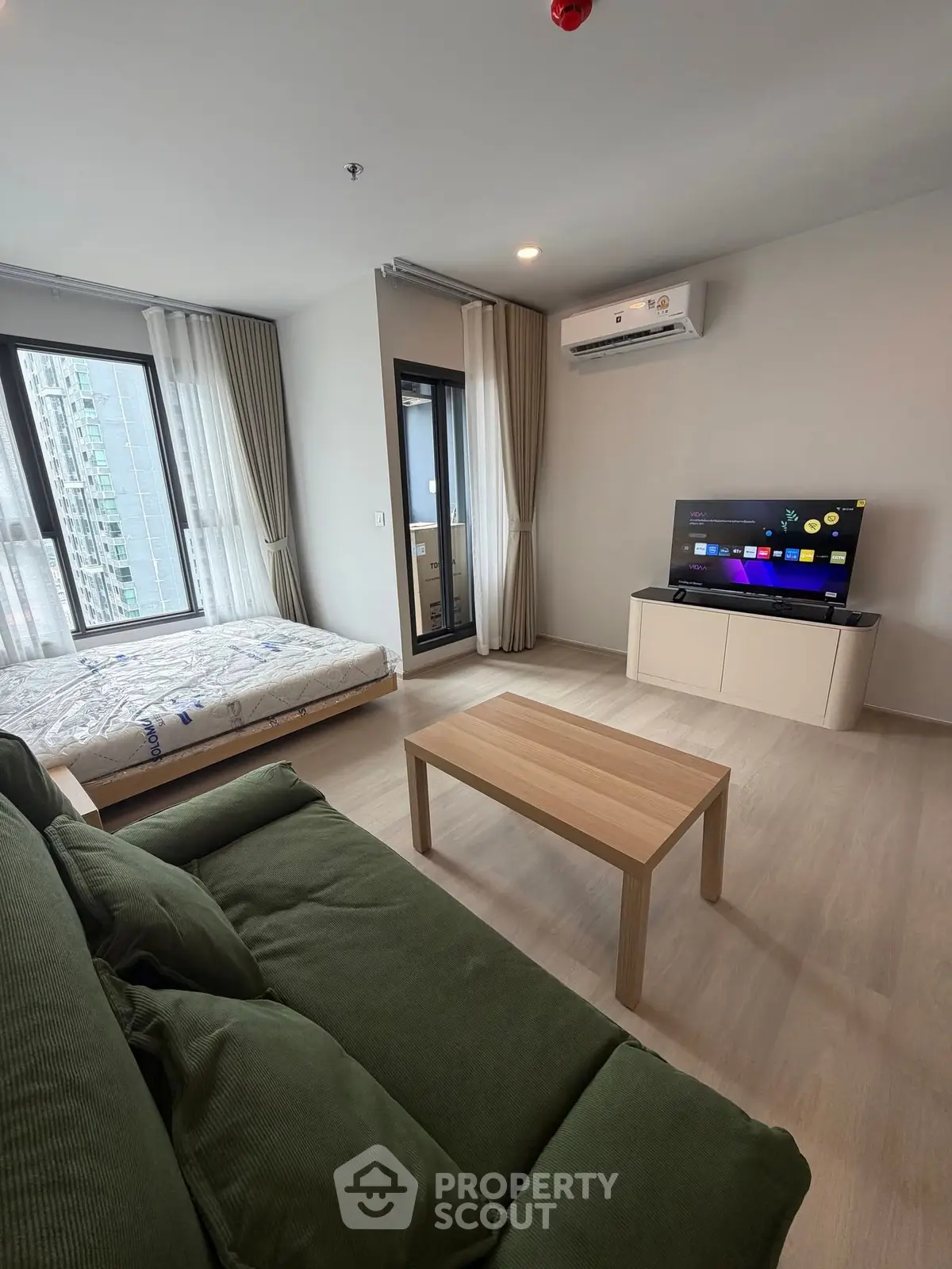 Modern living room with green sofa, wooden coffee table, and wall-mounted TV in a bright apartment.