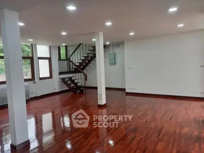 Spacious open-plan living area with polished hardwood floors and modern staircase.