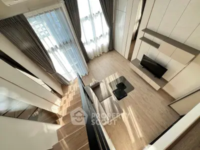 Modern living room with high ceiling and large windows, featuring stylish furniture and natural light.