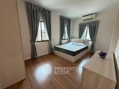 Spacious bedroom with wooden flooring and modern furnishings in a well-lit apartment.