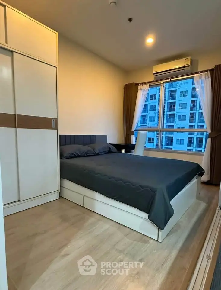 Modern bedroom with large window and city view, featuring sleek furniture and cozy ambiance.