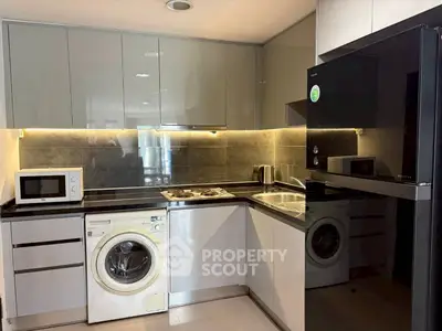 Modern kitchen with sleek cabinetry, washing machine, and microwave in a stylish apartment.