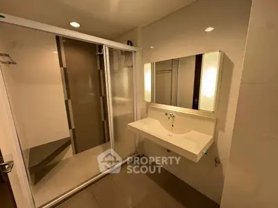 Modern bathroom with sleek shower and illuminated mirror in contemporary apartment.