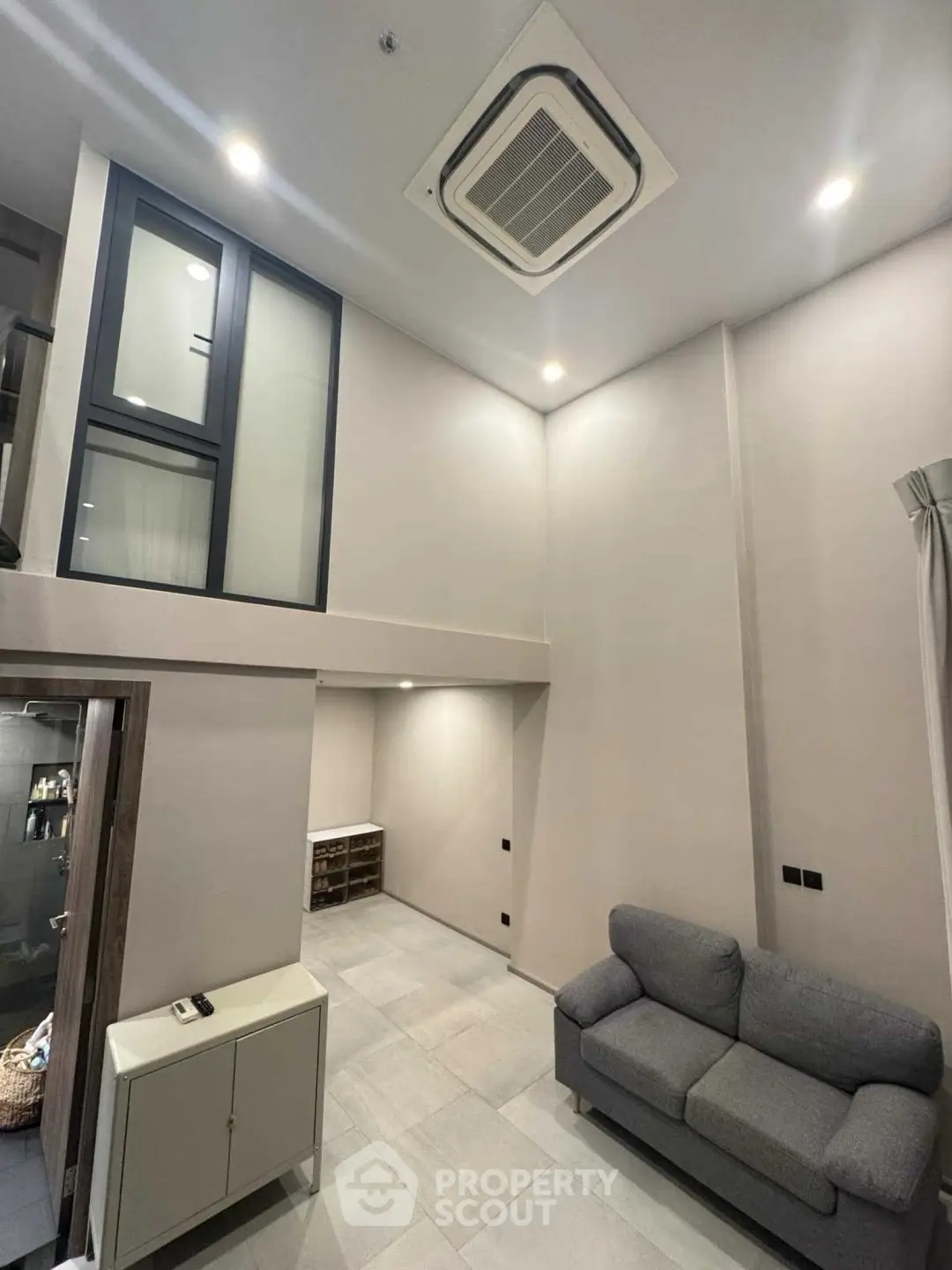 Modern living room with high ceiling and minimalist design, featuring a cozy gray sofa and sleek air conditioning unit.