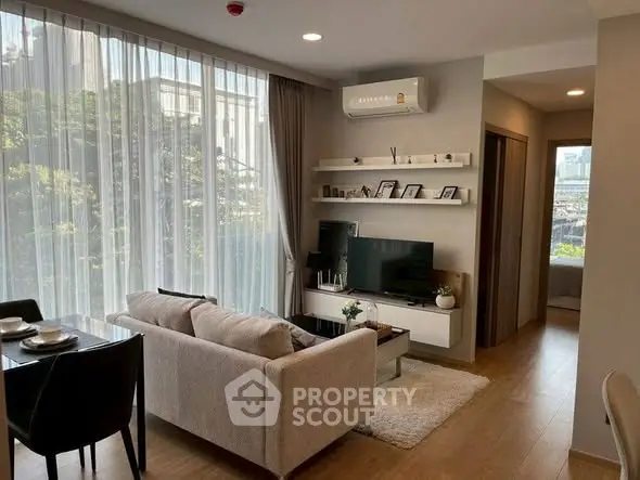 Modern living room with large windows, cozy seating, and stylish decor in a contemporary apartment.