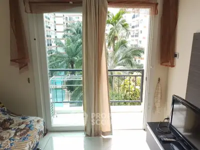 Cozy living room with balcony view overlooking lush greenery and modern apartment complex.