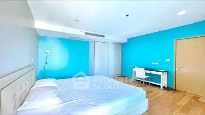 Spacious modern bedroom with vibrant blue accent wall and sleek wooden flooring.