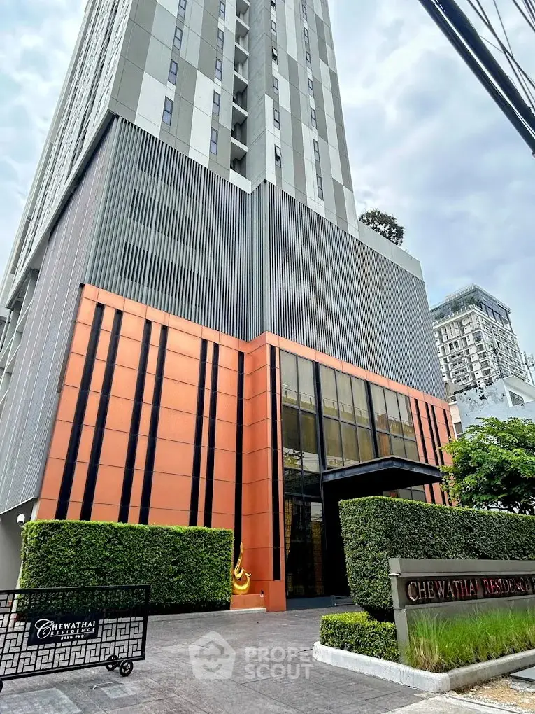 Modern high-rise building exterior with sleek design and lush greenery at entrance.