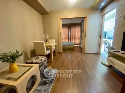 Modern living room with wooden flooring and cozy decor leading to a bedroom with natural light.