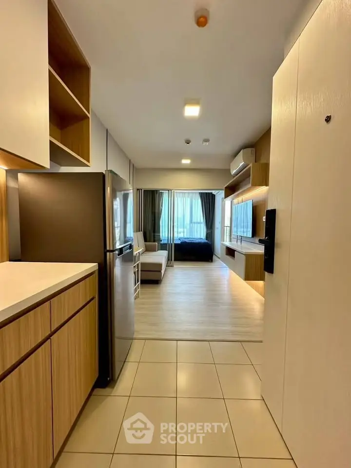 Modern open-layout apartment with sleek kitchen and cozy living area, featuring stylish wood cabinetry and ample natural light.