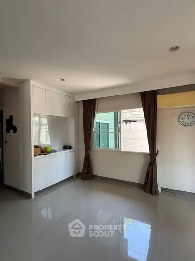 Spacious living room with large window and modern cabinetry in a bright apartment.