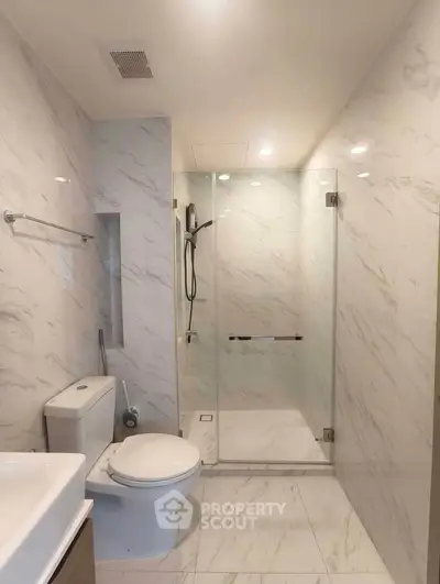 Modern bathroom with glass shower and marble tiles in luxury apartment.