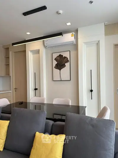 Modern living room with sleek furniture and stylish decor, featuring a glass dining table and contemporary lighting.