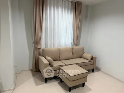 Cozy living room with beige sofa and matching ottoman, elegant curtains, and tiled flooring.
